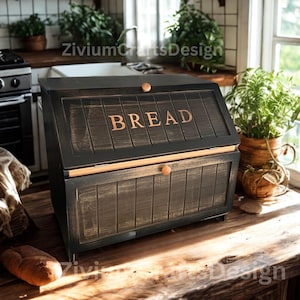 May include: A black wooden bread box with the word "BREAD" in copper-colored letters on the front. The box has a distressed finish and a wooden knob. The bread box is on a wooden surface.