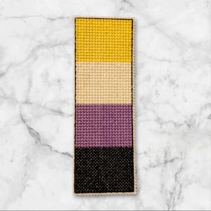 Puede incluir: Un marcapáginas con los colores de la bandera del orgullo no binario. La bandera es amarilla, blanca, morada y negra.