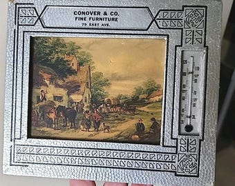 Termómetro publicitario antiguo con escena de pueblo en la tienda de muebles finos Conover.