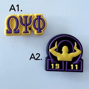 Peut inclure: Deux breloques pour chaussures. A1 présente les lettres grecques Oméga, Psi et Phi en violet sur fond jaune. A2 est un emblème circulaire noir et violet avec une silhouette jaune d'une personne aux bras levés et les chiffres 19 et 11 en jaune.