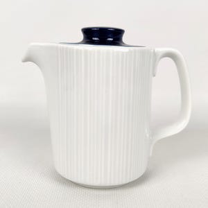 Op de afbeelding: Witte keramische creamer met een geribbelde textuur en een donkerblauwe deksel. De creamer heeft een gebogen handvat en een schenktuit. Een klassiek ontwerp voor het serveren van room of melk.