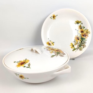 May include: White ceramic serving bowl with lid and a matching plate. Both pieces feature a yellow and green floral design. The bowl has a handle and a white lid with a small handle. The plate is round.