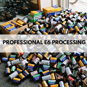 May include: A large collection of assorted 35mm film canisters, including Kodak Ektachrome, Fujichrome Velvia, and Agfa CTprecisa, scattered in cardboard boxes and on the floor, with the text PROFESSIONAL E6 PROCESSING overlaid.