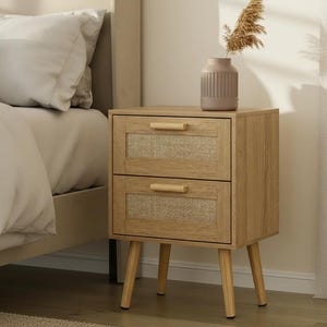 May include: A light wood nightstand with two drawers featuring woven cane panels and wooden handles. The nightstand has tapered legs and a vase with dried flowers on top. The bed and bedding are visible in the background.
