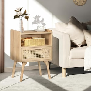May include: A light wood nightstand with a woven drawer and a shelf. A decorative vase with flowers and a wicker basket sit on the nightstand. The nightstand has angled legs and is next to a sofa.