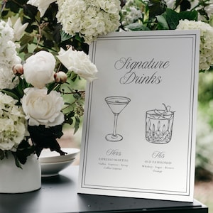 Puede incluir: Un letrero rectangular blanco con borde negro que presenta el texto Signature Drinks, con dibujos lineales de una copa de martini y un vaso bajo. Debajo de los dibujos, el texto indica Hers Espresso Martini y His Old Fashioned con ingredientes.