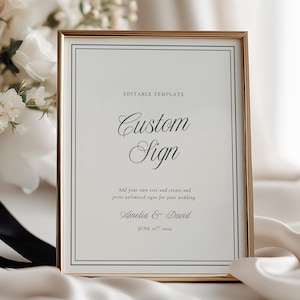 May include: A gold framed sign with the words "Custom Sign" in elegant script. The sign includes the text "Amelia & David" and "June 16th 2024". A bouquet of white and blush flowers is in the background.