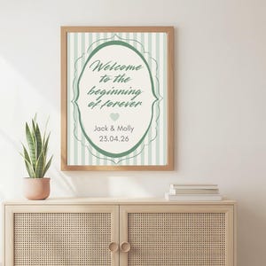 Può includere: Una stampa da parete incorniciata con uno sfondo a righe verticali verde chiaro e bianco e una cornice ovale decorativa centrale. Il testo recita Welcome to the beginning of forever, Jack & Molly, e 23.04.26, con una piccola icona a cuore.