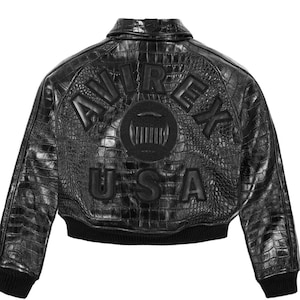 Könnte beinhalten: Schwarze Leder-Bomberjacke mit Krokodiltextur. Auf der Rückseite stehen die Worte "AVIREX USA" in erhabenen Buchstaben mit einem kreisförmigen Emblem. Die Jacke hat einen gerippten Kragen, Bündchen und Saum.