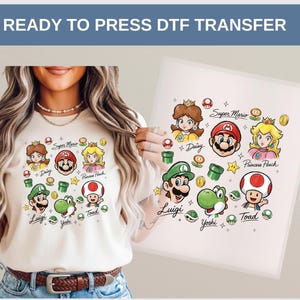 May include: Cream-colored t-shirt featuring a colorful Super Mario design with characters like Mario, Luigi, Princess Peach, and Toad. The design includes the text "Super Mario", "Daisy", "Princess Peach", "Luigi", "Yoshi", and "Toad".