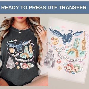 May include: A dark gray t-shirt featuring a colorful graphic design with the text "EPIC UNIVERSE". The design includes cartoon characters, a castle, a dragon, and the Super Mario Bros. characters. The words "READY TO PRESS DTF TRANSFER" are at the top.