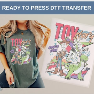 May include: A dark green t-shirt featuring a colorful graphic of Toy Story characters, including Woody, Buzz Lightyear, and Rex. The design includes the text "TOY STORY" and "SINCE 1995". The image also shows a DTF transfer.