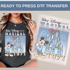 Może przedstawiać: Ciemnoszara koszulka z nadrukiem w stylu retro przedstawiającym Myszka Miki przed zamkiem Kopciuszka, z napisem "Walt Disney World MAGICAL Since 1971." Widoczny jest r&oacute;wnież transfer DTF gotowy do prasowania.