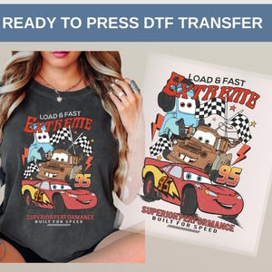 May include: A charcoal gray t-shirt with a colorful graphic of cartoon race cars and the text "LOAD & FAST EXTREME". The design includes the number "95" and the words "SUPERIOR PERFORMANCE BUILT FOR SPEED".