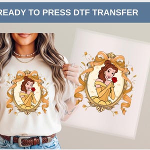 Op de afbeelding: Een cr&egrave;mekleurig T-shirt met een DTF-transfer van een cartoonprinses in een gouden lijst, met een rode roos. De woorden "READY TO PRESS DTF TRANSFER" staan bovenaan. De prinses draagt een gele jurk en handschoenen.