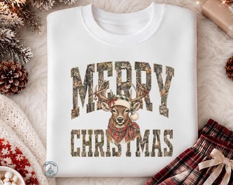 May include: A white crewneck sweatshirt featuring the text MERRY CHRISTMAS in a camouflage pattern. Centered between the words is an illustration of a deer wearing a plaid scarf and a green and white buffalo check beanie with a pom-pom.