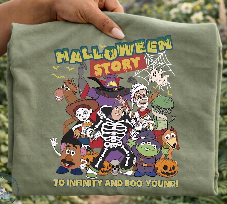 May include: An olive green t-shirt featuring a graphic of Toy Story characters in Halloween costumes, including a skeleton Buzz Lightyear, with the text HALLOWEEN STORY and TO INFINITY AND BOO YOUND printed in yellow and white lettering.