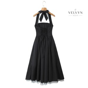 May include: Black halter dress with a bow at the neck and a corset-style back. The dress has a full skirt and is hanging on a wooden hanger. The brand name "VELVYN NOIR" is printed on the right side of the image.