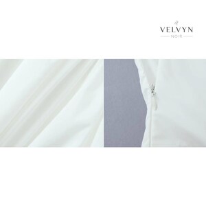 May include: Close-up of a white garment with a zipper detail. The fabric has a subtle sheen and is draped in soft folds. The brand name "VELVYN NOIR" is displayed in elegant typography.