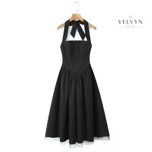 May include: A black halter dress with a bow detail at the neckline, hanging on a wooden hanger. The dress has a square neckline and a flared skirt. The brand name "VELVYN NOIR" is printed on the right side.