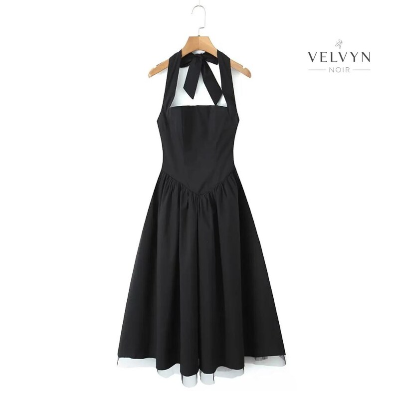 May include: A black halter dress with a bow detail at the neckline, hanging on a wooden hanger. The dress has a square neckline and a flared skirt. The brand name "VELVYN NOIR" is printed on the right side.