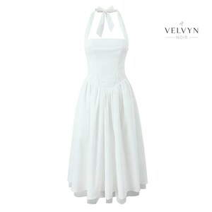 May include: A white halter dress with a square neckline and a flowing skirt. The dress features a bow at the halter neck and a fitted bodice. The brand name "VELVYN NOIR" is displayed in black text on the right side of the dress.