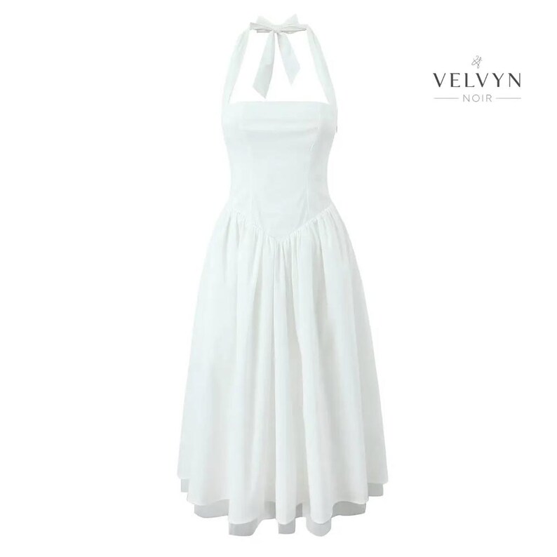 May include: A white halter dress with a square neckline and a flowing skirt. The dress features a bow at the halter neck and a fitted bodice. The brand name "VELVYN NOIR" is displayed in black text on the right side of the dress.