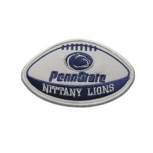 Pode incluir: Remendo bordado em forma de bola de futebol americano. O remendo é branco com uma borda azul marinho e apresenta as palavras "Penn State Nittany Lions" em azul marinho. O logotipo da Penn State está no centro.
