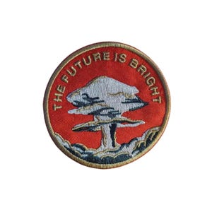 May include: Round embroidered patch with a red background and a tree design. The text "THE FUTURE IS BRIGHT" is embroidered in gold around the edge of the patch. The tree is white and black.