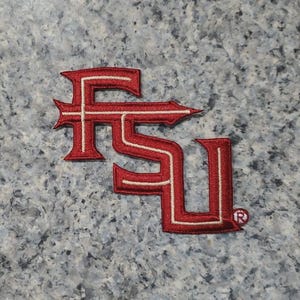 Può includere: Toppa ricamata con le lettere "FSU" in rosso granato con dettagli bianchi. La toppa ha un design decorativo e un simbolo di marchio registrato. Ideale per giacche, borse o altri articoli in tessuto.