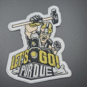 May include: Embroidered patch showing a cartoon construction worker with a hammer, wearing a hard hat. The patch has the words "LET'S GO! PURDUE" in yellow and white. The patch is outlined in white.