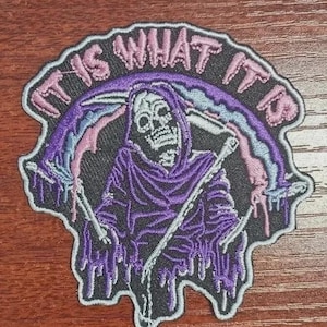 Op de afbeelding: Geborduurde patch met een Grim Reaper in een paarse capuchon, met een zeis. De patch heeft een zwarte achtergrond met de tekst "IT IS WHAT IT IS" in roze en paars. Het ontwerp bevat een regenboog.