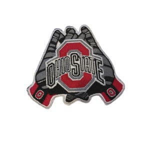 Può includere: Toppa ricamata con il logo della Ohio State University. La toppa ha un centro rosso e bianco con le parole "OHIO STATE" in un carattere stilizzato. La toppa è circondata da un design grigio e nero, con accenti rossi.