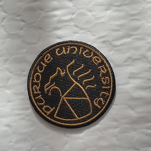 May include: Round black embroidered patch with gold-colored text and design. The text reads "purdue university" around the edge. The design in the center features a stylized eagle and a triangle.