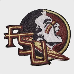 Può includere: Toppa ricamata con le lettere "FS" in granato e oro, con un logo a forma di testa di Seminole. La toppa ha uno sfondo nero con un bordo granato e oro. La testa di Seminole è bianca con dettagli rossi e oro.