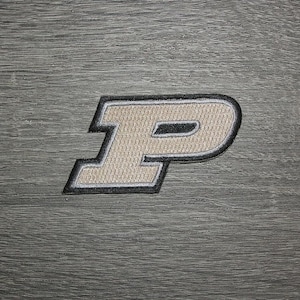 May include: Embroidered patch with the letter "P". The letter is beige with a black outline and a white border. The patch is set against a grey, wood-grain background. Ideal for clothing or accessories.