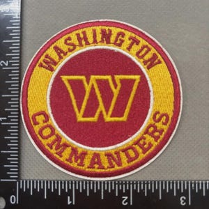 May include: Embroidered patch featuring the Washington Commanders logo. The patch is circular, with a red center and a yellow border. The team name and logo are prominently displayed.