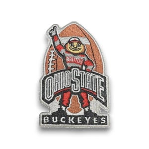 Può includere: Toppa ricamata con la mascotte degli Ohio State Buckeyes, Brutus, in abito rosso e grigio, con uno sfondo di football. La toppa include le parole "OHIO STATE" e "BUCKEYES".