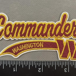 May include: Embroidered patch featuring the word "Commanders" in a script font, with "WASHINGTON" below. The patch includes a stylized "W" and is in burgundy and gold colors.