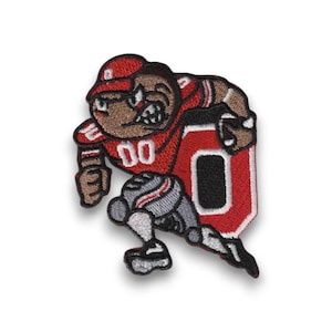 Può includere: Toppa ricamata raffigurante un giocatore di football americano dei cartoni animati in uniforme rossa con il numero "00". La toppa ha uno sfondo bianco e un contorno nero. Il giocatore corre con un pallone.