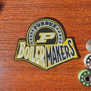 May include: A white ceramic mug with a black handle and the text "But First, Coffee" in a bold, black font. The mug is set against a blurred background, suggesting a cosy setting.