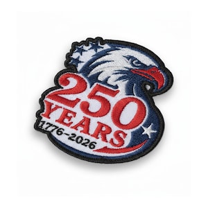 Puede incluir: Parche bordado con un diseño patriótico. Presenta una cabeza de águila azul, blanca y roja, con el texto "250 YEARS 1776-2026". El parche tiene un borde negro y estrellas, celebrando un aniversario significativo.