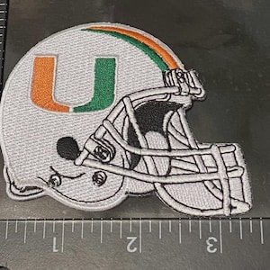 May include: Embroidered patch of a gray football helmet with a white face mask. The helmet features a large orange and green "U" logo. The top of the helmet has an orange and green stripe. The patch is approximately 3 inches wide.