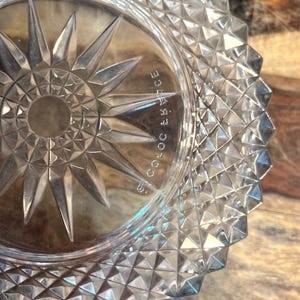 May include: Clear glass dish with a starburst design in the centre and a geometric pattern around the rim. The dish has the text "S. COLOC FRANCE" etched on the side.