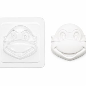 May include: A clear plastic mold featuring a cartoon turtle face design alongside a solid white cast of the same turtle face. The mold is square-shaped with rounded corners, while the cast is shaped to the outline of the turtle's head.