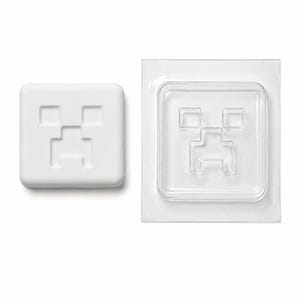 Peut inclure: Un savon carré blanc présentant un motif de visage pixélisé en creux, accompagné d'un moule en plastique transparent assorti. Le savon a des coins arrondis et une finition mate lisse, tandis que le moule transparent affiche le même motif.