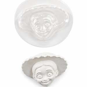 Peut inclure: Un moule en plastique transparent présentant le visage en relief d'un personnage portant un chapeau à larges bords, placé au-dessus d'un moulage blanc solide du même visage, révélant les détails du visage et la texture du chapeau.