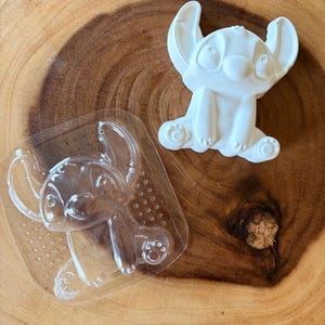 May include: A clear plastic mould featuring the shape of a cartoon character with large ears and a sitting posture, accompanied by a solid white plaster casting of the same character design, showing the detailed facial features and paw pads.