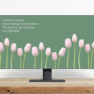 Könnte beinhalten: Ein Computermonitor zeigt einen grünen Hintergrund mit rosa und weißen Tulpen. Der weiße Text lautet: "rooted in grace, flourishing in abundance, The Lord is my portion, so I REJOICE". Der Monitor steht auf einer Holzoberfläche.