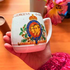 May include: White ceramic mug featuring a royal emblem with portraits and the text "G-GEORGE VI & QUEEN". The mug has a handle and is decorated with a crown, laurel branches, and the motto "DIEU ET MON DROIT".